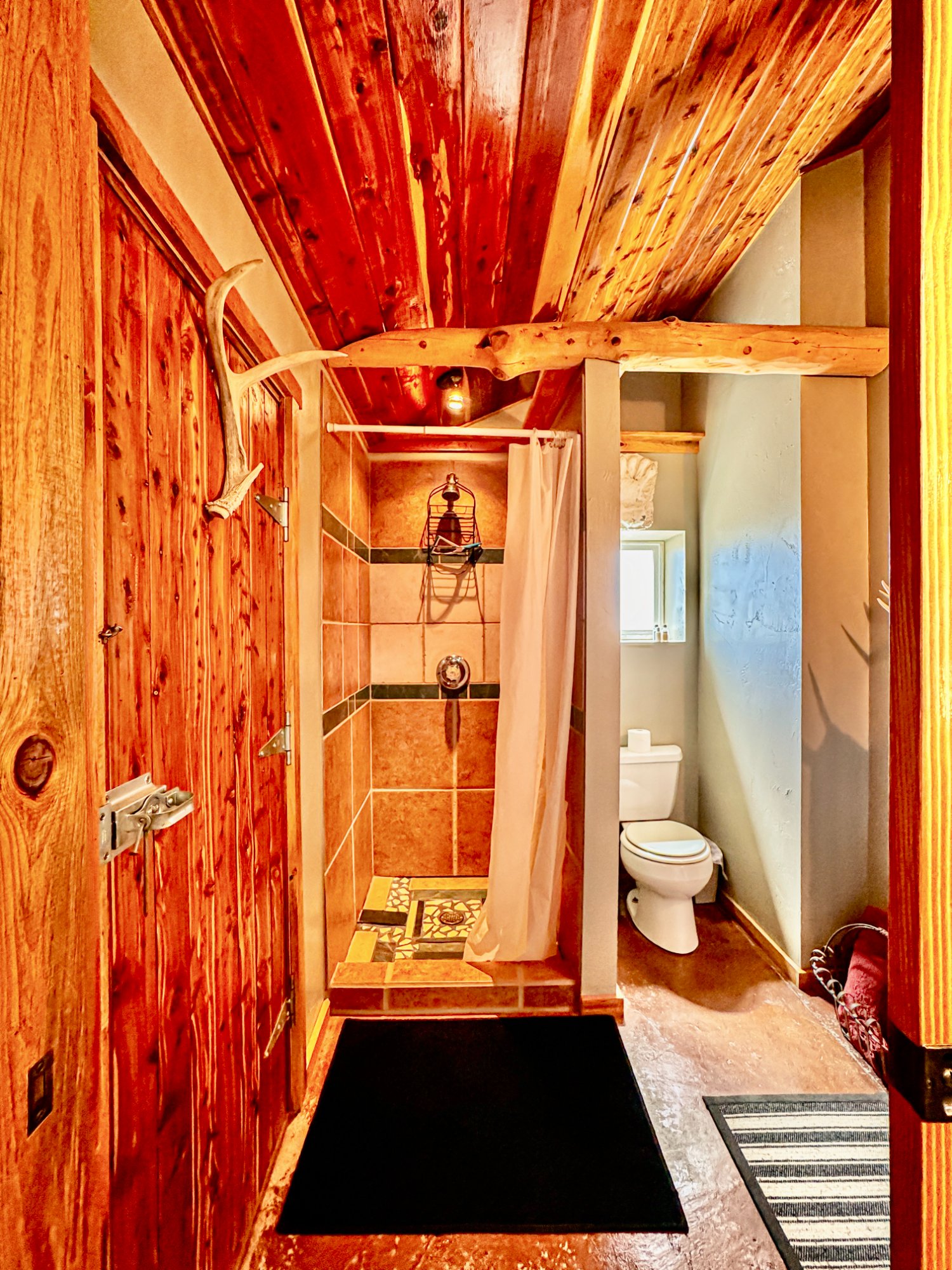 Bathroom with tile shower, antler door handle, and cedar ceiling